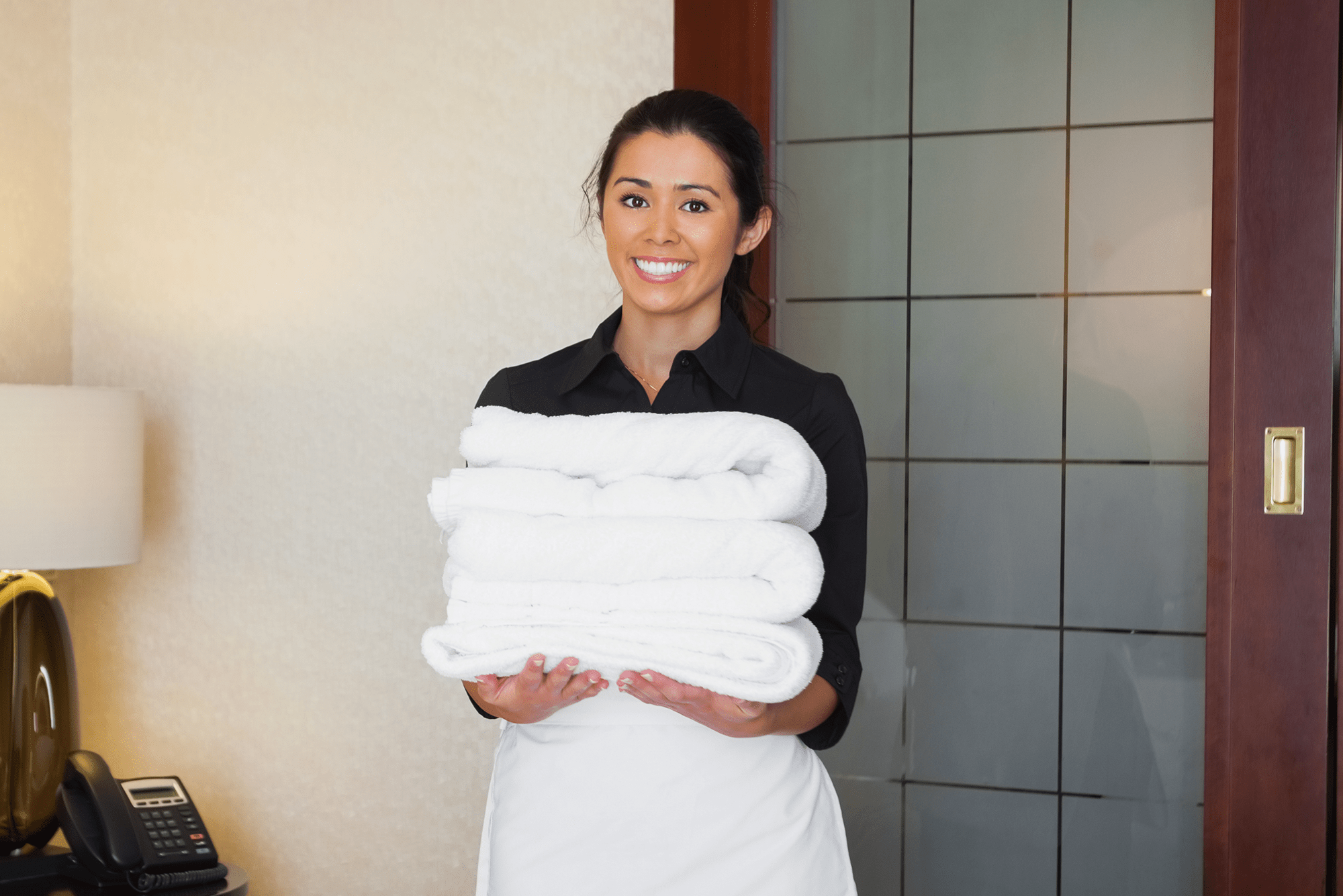 Female housekeeper smiling at the camera and holding white towels