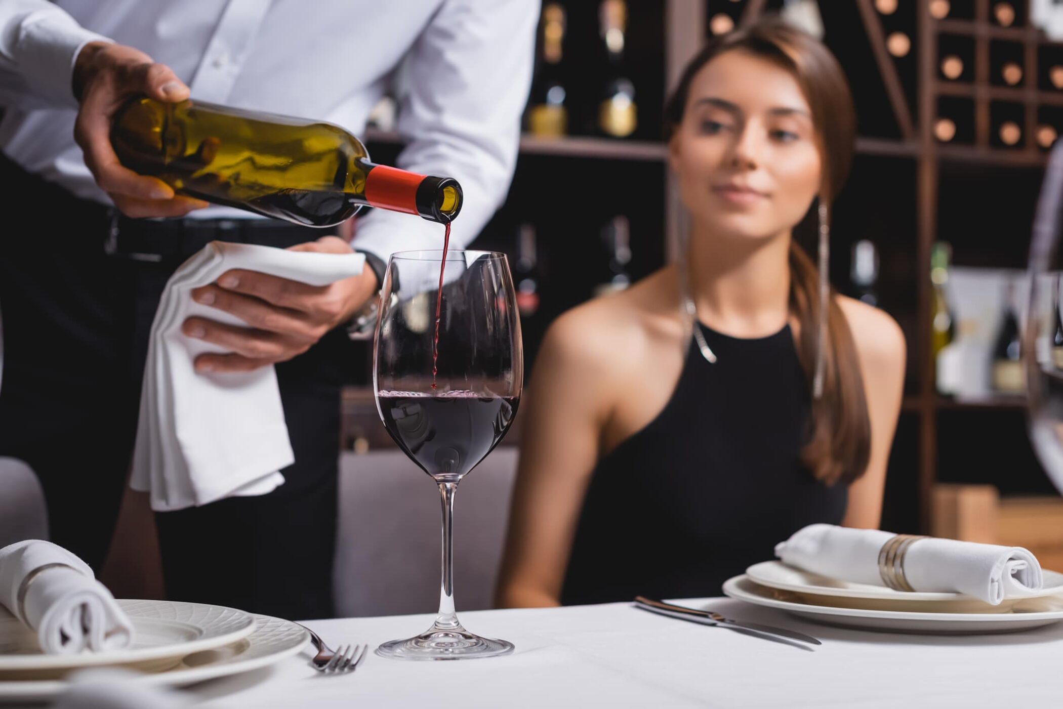 Selective focus of a waiter pouring wine near woman at table in restaurant