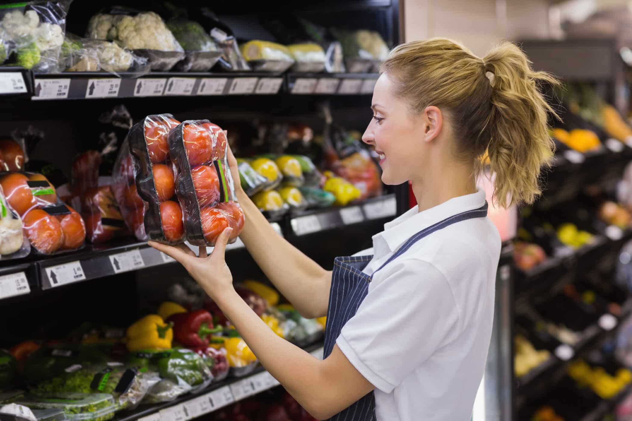 Side view of a smiling blonde retail assistant worker taking a tomatoes